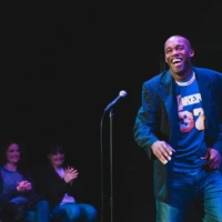 Nnamdi smiling on stage. He is wearing a blue American Football jersey with the number 32 on the front.